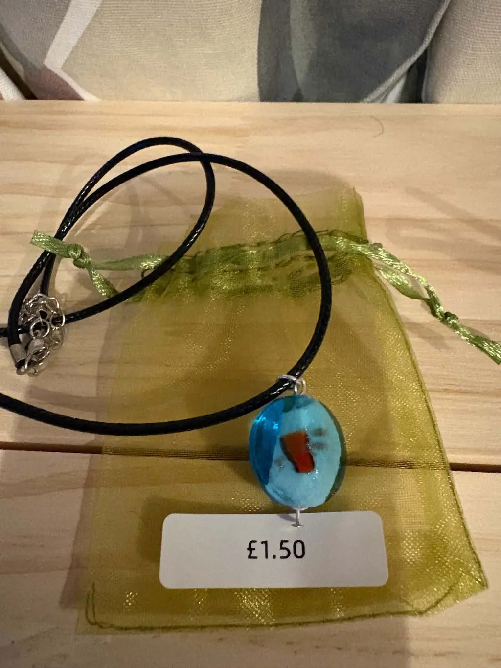 A round turquoise glass pendant on a black cord, on a green organza bag