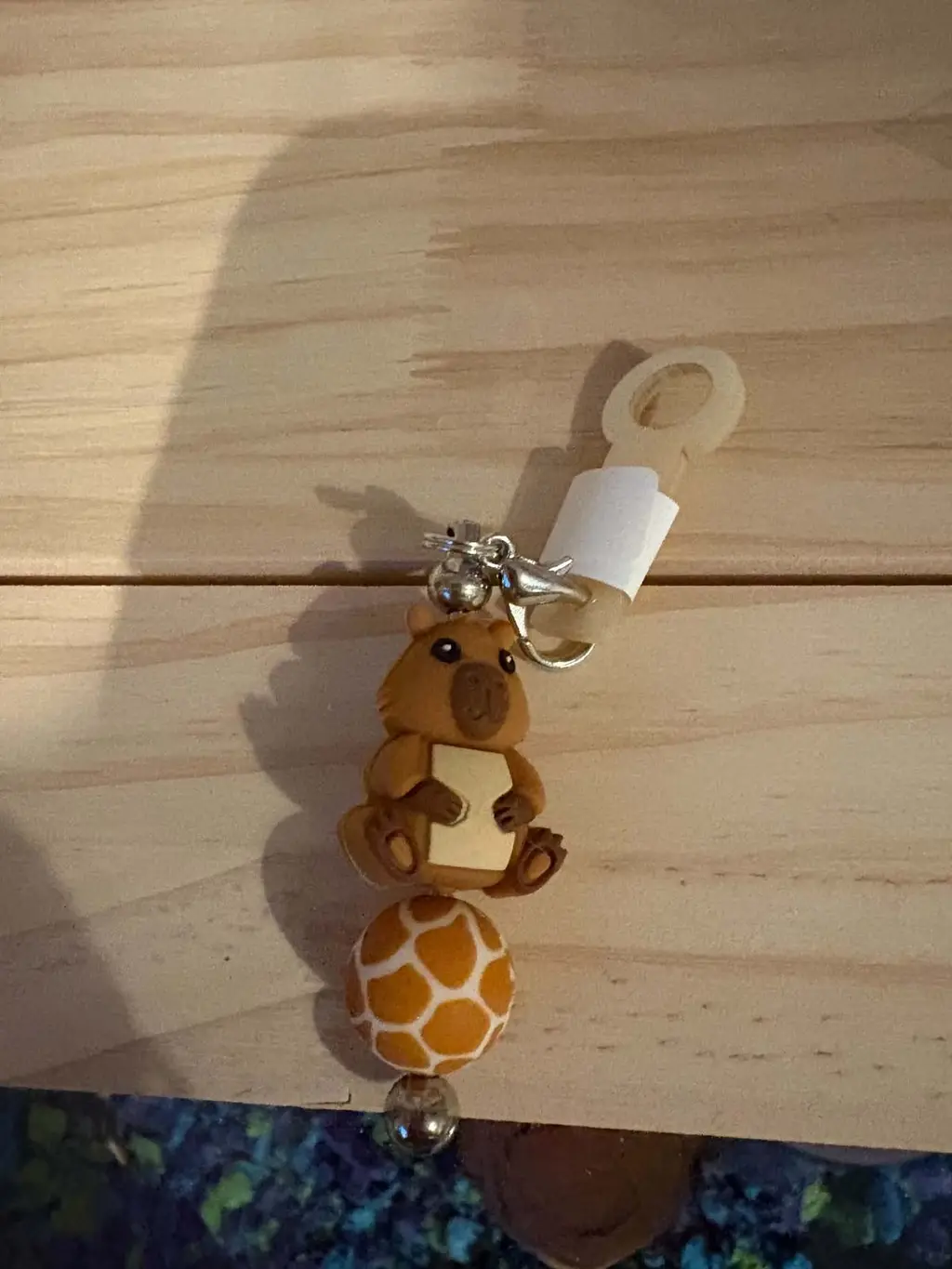 A capybara charm with a giraffe-print bead, a little bell and a clip