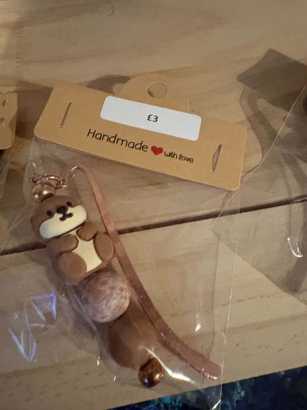 A rose gold bookmark with a brown clay otter charm on a Handmade with love card